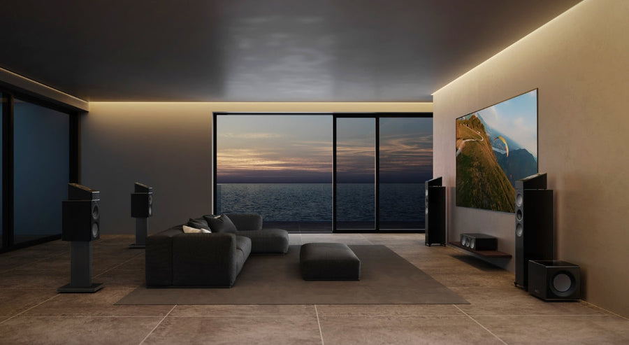 Luxe, moderne woonkamer met KEF-vloerstaande luidsprekers, wandgemonteerde tv en uitzicht op de oceaan via kamerhoge ramen, ontworpen voor een meeslepende thuisbioscoopervaring.