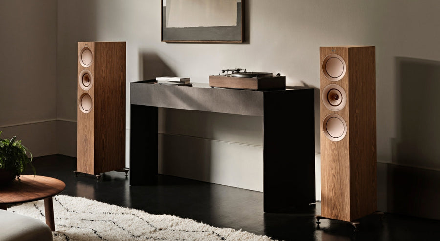 KEF-vloerstaande luidsprekers met een natuurlijke houtafwerking, gecombineerd met een platenspeler op een minimalistische zwarte consoletafel, in een moderne luisterruimte.
