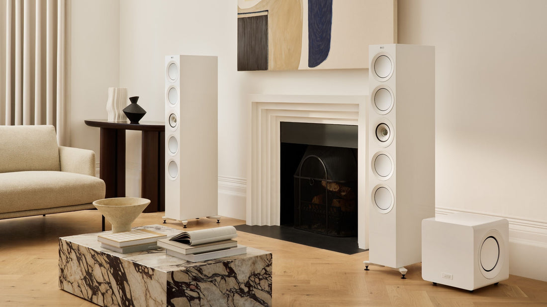 A living room scene showcasing a fireplace, a plush couch, and a white KEF R11 Meta HiFi Speaker positioned nearby with a with KC92 subwoofer