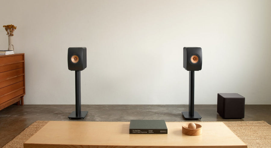 KEF boekenplankluidsprekers op standaards met compacte zwarte subwoofer in een minimalistische moderne woonkamer